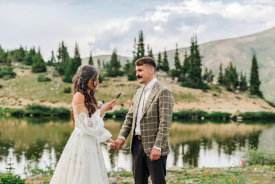 couple standing in the forest together, there is fog and green grass. the groom is kissing the bride on the head