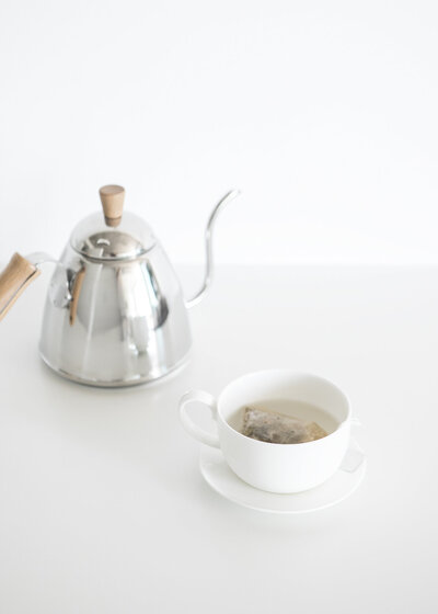 silver tea kettle and white cup of tea on white counter
