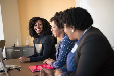 Vanessa leads a workshop, interacting with attendees seated around a table, highlighting her role as a dynamic facilitator.