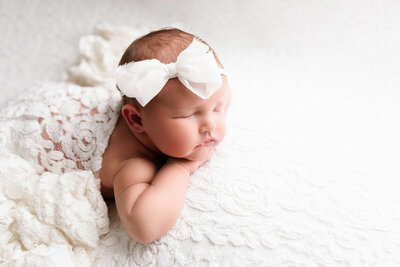 newborn baby on bright white blanket with bow