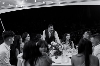 A newlywed standing at a table of wedding guests and laughing with them 