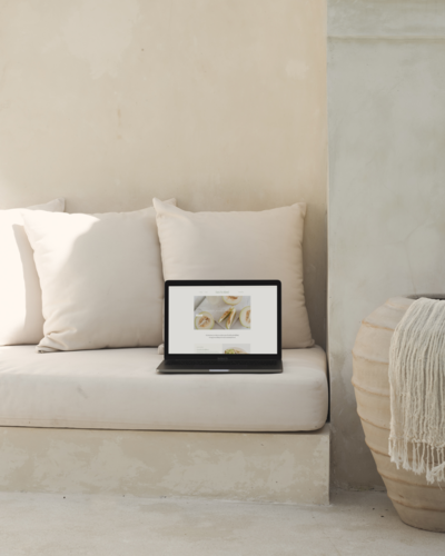a laptop displaying a website on a neutral-toned couch with beige pillows, in a modern and minimalist setting.