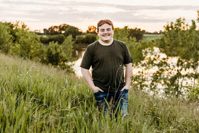teen boy standing in tall grasses next to a pond