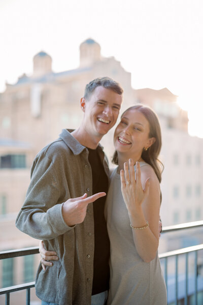 Couple celebrating engagement at The Pearl in San Antonio, showing ring and smiling on a balcony at sunset.