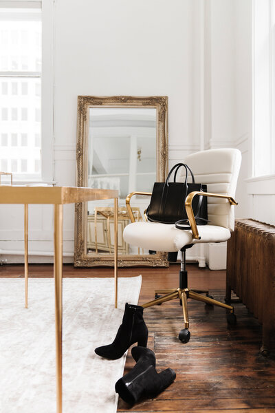 Modern feminine home office with neutral tones, gold swivel chair, full-length mirror, and stylish black handbag—a creative workspace for women entrepreneurs.
