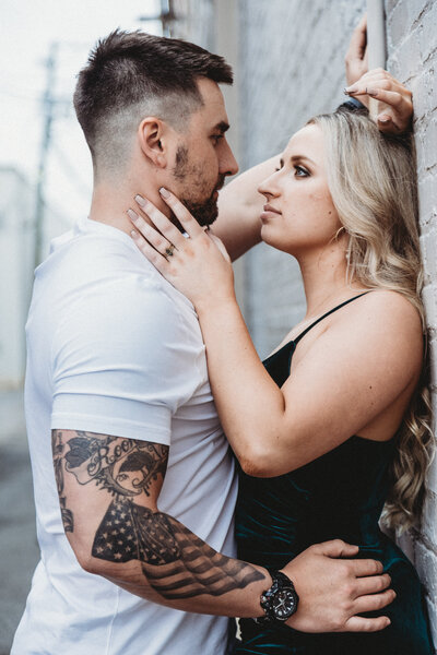 Casual couple with tattoos  pose against brick wall for engagement photos.