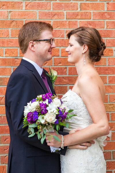 Bride and Groom smiling while facing each other in front of red brick wall