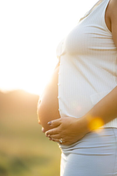 profile shot of a pregnant woman's baby bump, holding her belly with both hands in glowy sunset lighting