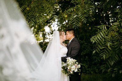 couple kissing under a tree on their wedding day beneath the veil