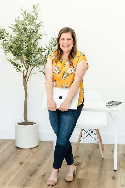 A web designer leaning on the desk, holding a laptop