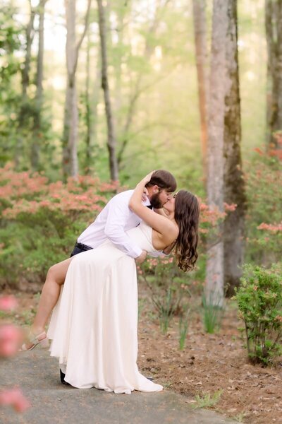 Future groom dips his bride to be for a kiss in the light filled woods of Callaway Gardens
