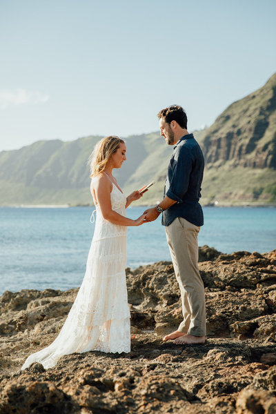 bride & groom standing on rocks next to ocean