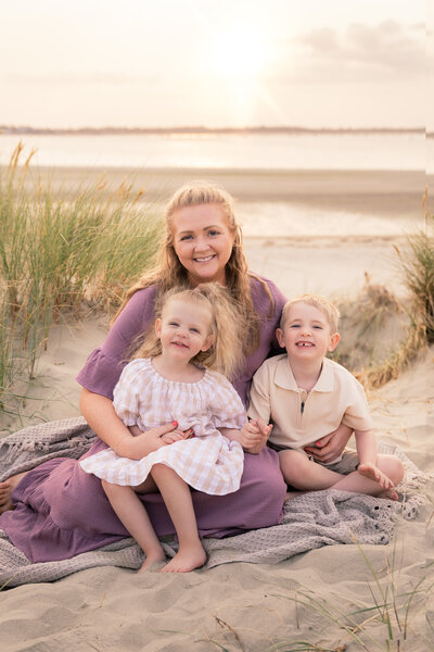 Mum with boy and girl, smiling at sussex family photographer on beautiful golden sunset beach