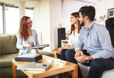Married couple sitting on a couch by a coffee table talking to a realtor.