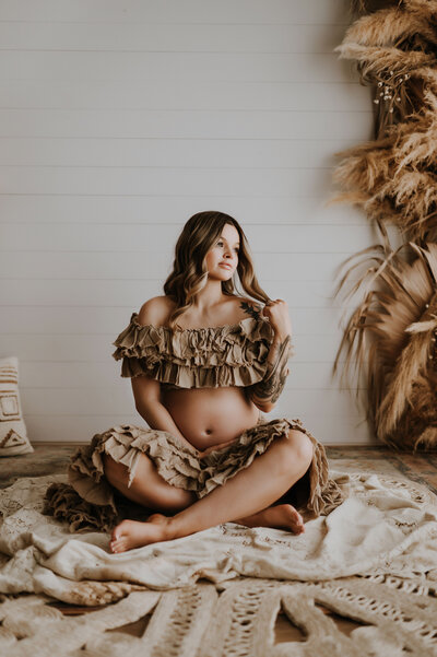 A pregnant woman sitting in a photography studio posing for maternity images