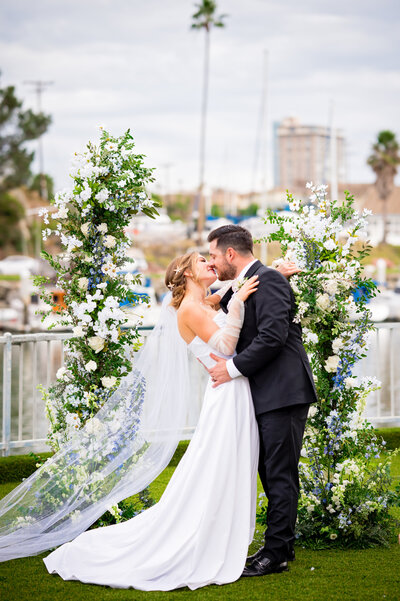 Luxury bride and groom kissing in front of modern floral archway