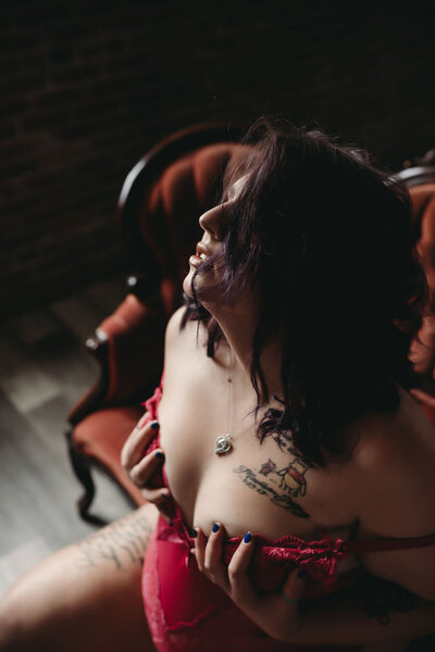 boudoir portrait of brunette woman with tattoos touching breasts in red lingerie