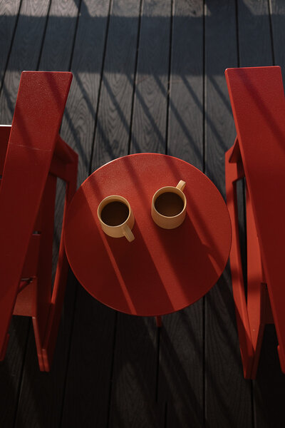 coffee cups on a small round red table in between red chairs