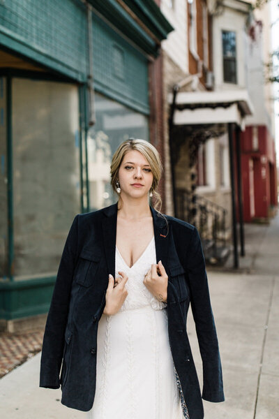 Bride staring into camera holding husbands  jacket around her shoulders