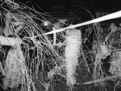 Black and white image of couple leaving wedding reception surrounded by streamers