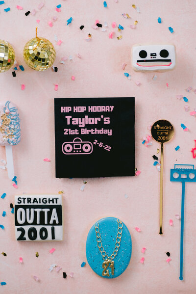 Flat lay featuring cassette tape favors, gold chains, and bold 90s graphics for a 21st birthday party