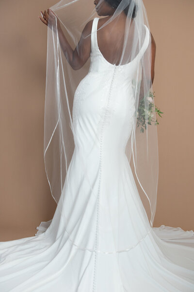 Bride wearing a floor length veil with ribbon edge and holding a white and blush bouquet