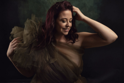 Inspired during her boudoir photoshoot a woman smiles in a green gown in Vancouver