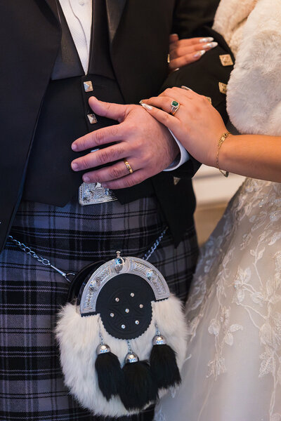 Close up of bride and groom's hands entwined that shows their wedding attire and his scottish sporan.