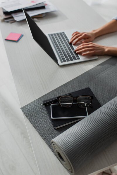 A woman's hands on a laptop next to a gray yoga mat