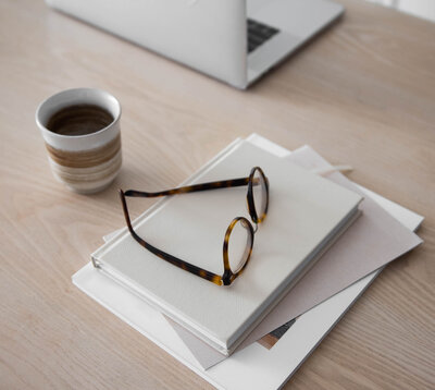 Desk in a creative studio with glasses, coffee a computer and books