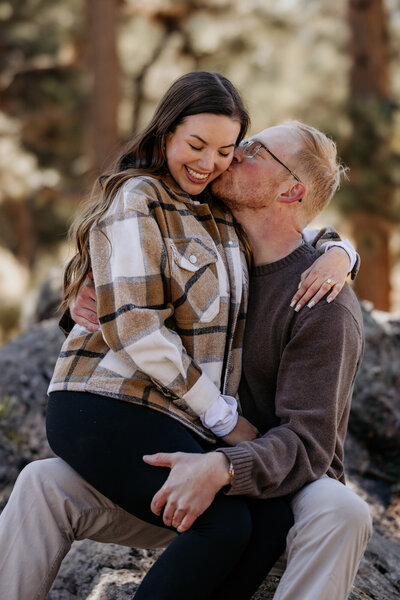 man and woman sit on rock in the Colorado mountains during engagement photo shoot.