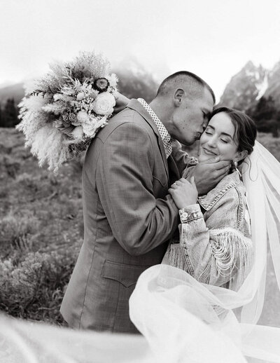 groom kissing bride on the cheek while they both embrace