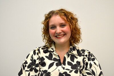 A portrait of Stella Winchester, a stylist at 212 Salon, Spa, & Barbershop, wearing a black and white floral top and smiling at the camera.