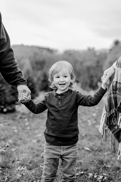 A young toddler boy being held by his parents and leaning over for a kiss