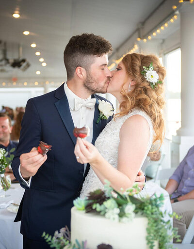 bride and groom kiss while holding strawberries at receoption