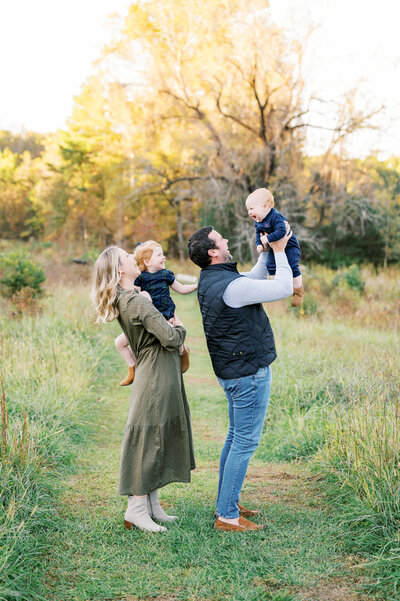 Family of four plays during photo session & dad lifts baby boy in the air
