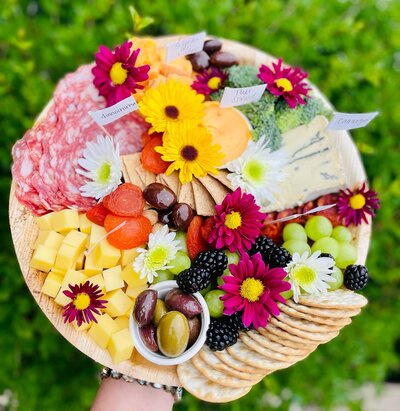 A round platter with charcuterie and flowers on top.