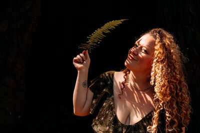 Spiritual and business witch coach Rachael Maddox holding a fern leaf, inviting powerhouse witches into Business Witchery’s CEO Coven, a year-long mastermind to birth bold, world-changing work.