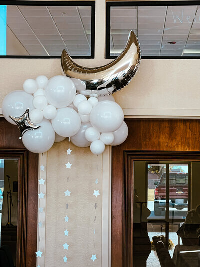 ballon art of silver moon and stars sitting on a white cloud with sparkles flowing underneath