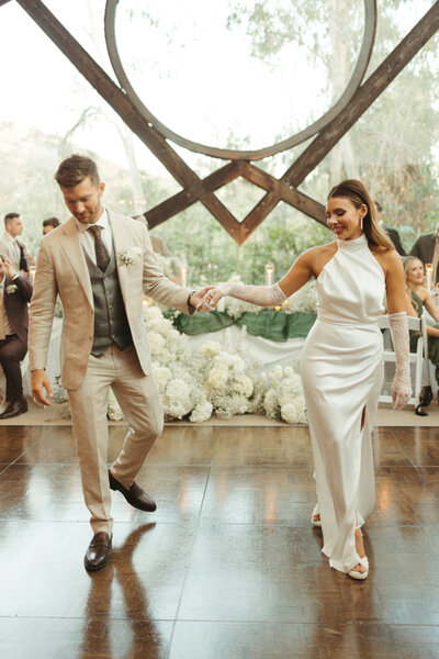 Young couple doing their first dance at Calamigos Ranch at the Oak Room in a white dress and tan suit 