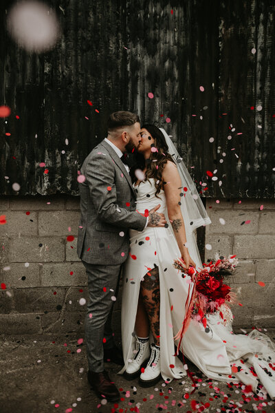 Tattooed couple kiss as confetti falls on them. 