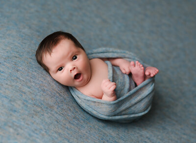 A tiny little newborn boy yawns during his newborn photography session.
