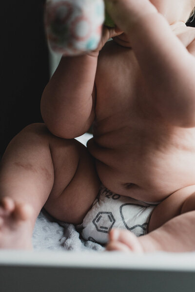 Baby sitting on changing table with teething toy in his diaper lifestyle newborn photography