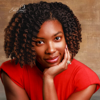 "A confident woman in a red dress poses for a professional portrait against a warm-toned studio backdrop, photographed by a Greenville SC photographer."