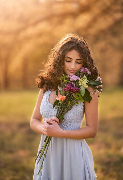 A beautiful high school senior smelling fresh flowers during her senior portrait session in Asheville NC