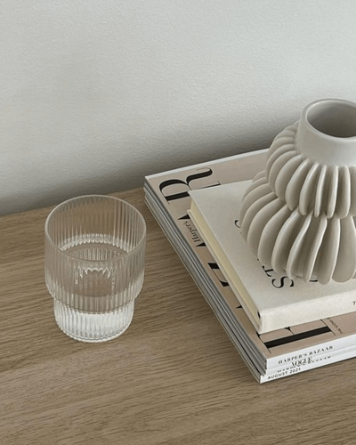 A tabletop featuring a stack of books, a unique ceramic vase, and a textured glass of water, styled in a minimalist aesthetic.