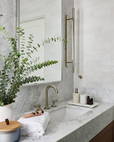 A luxury bathroom vanity with a marble countertop and soap bottles, brushed nickel fixtures, a large mirror, and potted plant