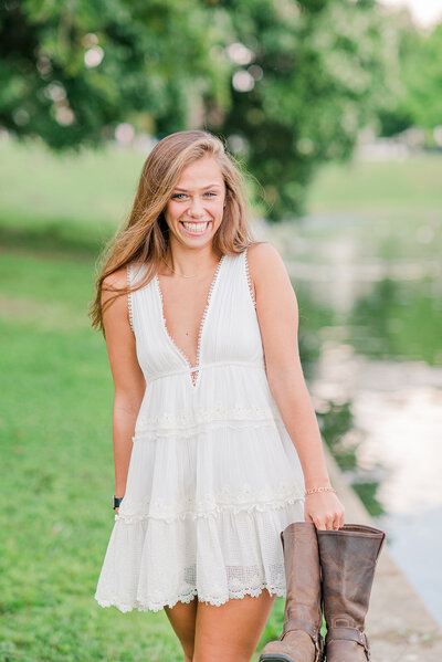 girl smiling in a white dress and holding cowgirl boots