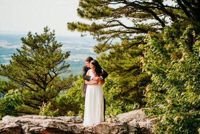 Couple hugging on wooded overlook surrounded by pine trees during mountain
elopement