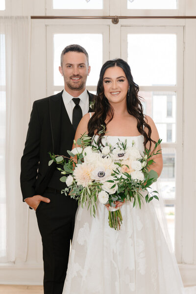 Portrait of bride and groom standing in front of glass french doors.